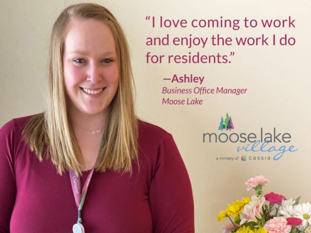 Ashley wearing magenta shirt, a pink lanyard. Moose Lake Village logo and quote, "I love coming to work and enjoy the work I do for residents."